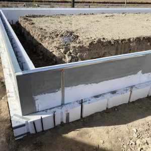 The image shows the foundation of a building under construction, with a square-shaped concrete base surrounded by insulated concrete forms. The area within the foundation is filled with compacted soil, ready for further construction.