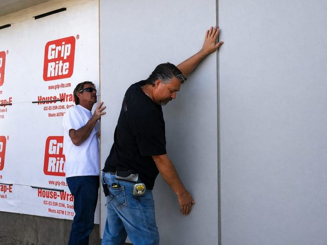 Contractors installing prefabricated insulated siding panels on exterior wall system.